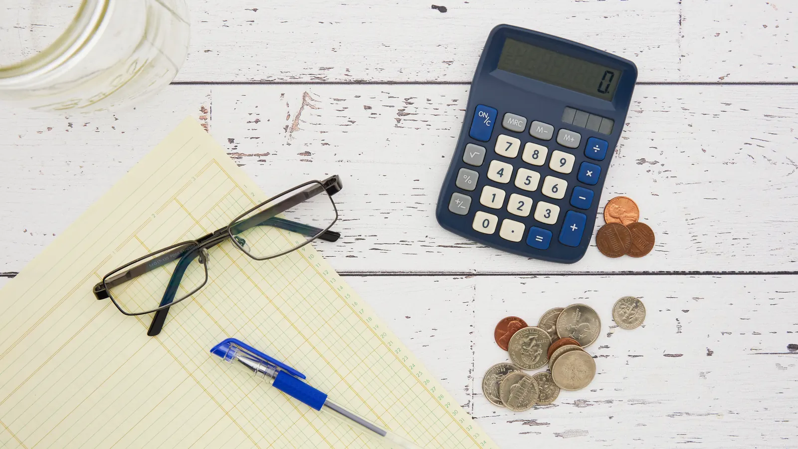 Calculator, coins, glasses and a notepad on a desk